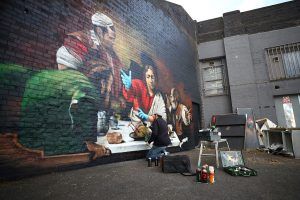 Artist Lionel Stanhope paints a mural in Ladywell depicting the Supper at Emmaus by Caravaggio with added protective gloves, following the outbreak of the coronavirus disease (COVID-19), London, Britain, May 5, 2020. REUTERS/Hannah McKay
